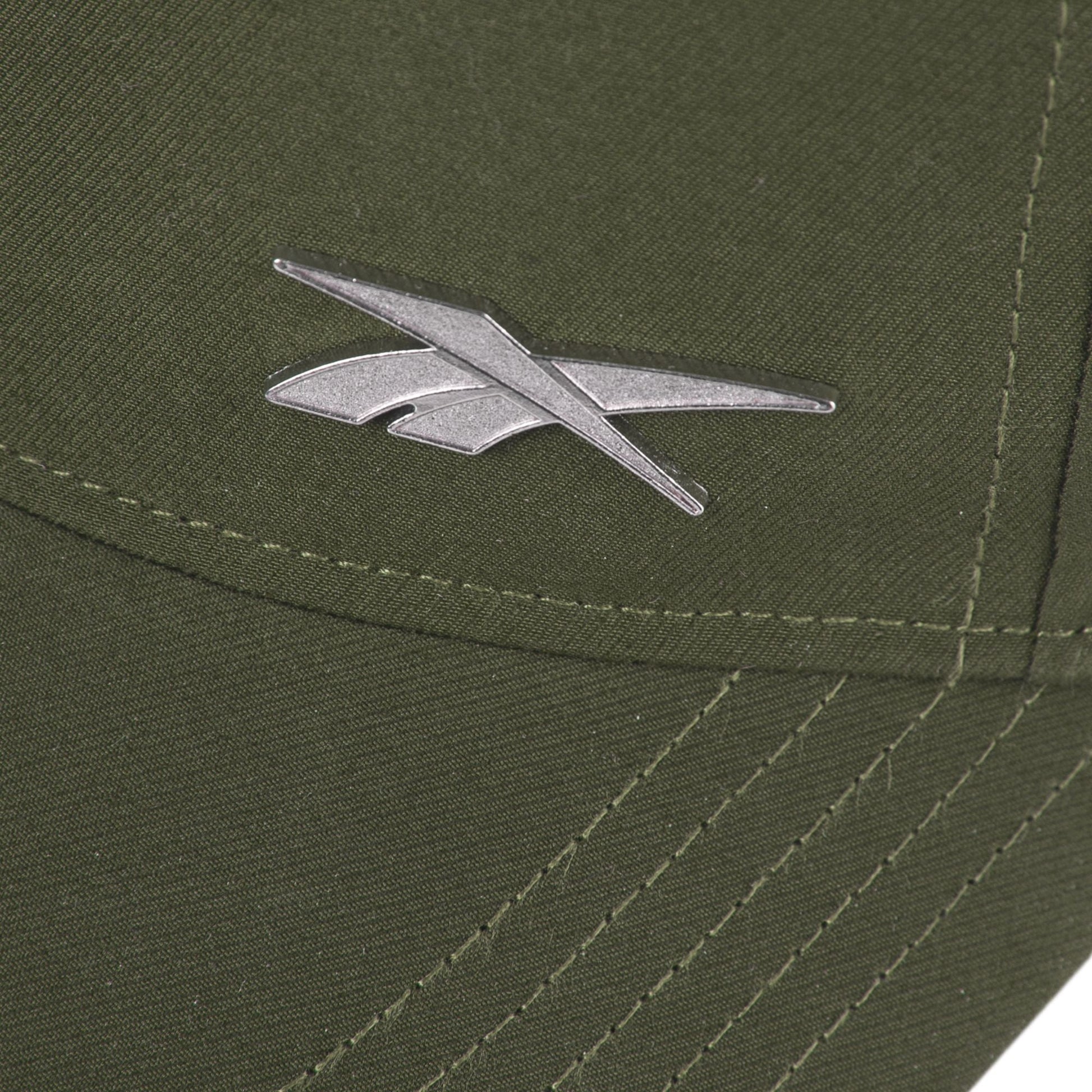 Close-up of the silver Reebok logo on olive green fabric of the Reebok Badge Cap, featuring visible stitching and intersecting seams.