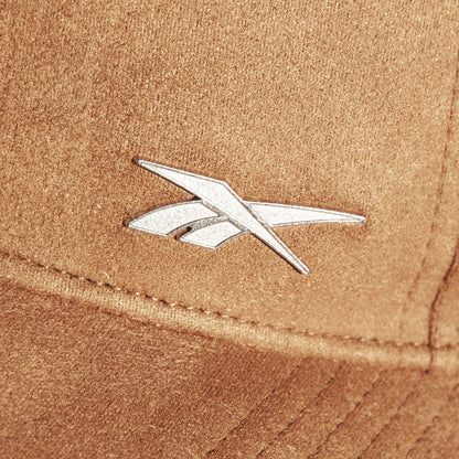 A close-up of the brown Suede Badge Cap by Reebok shows a silver, angular metallic logo, giving this vegan suede cap a modern look.