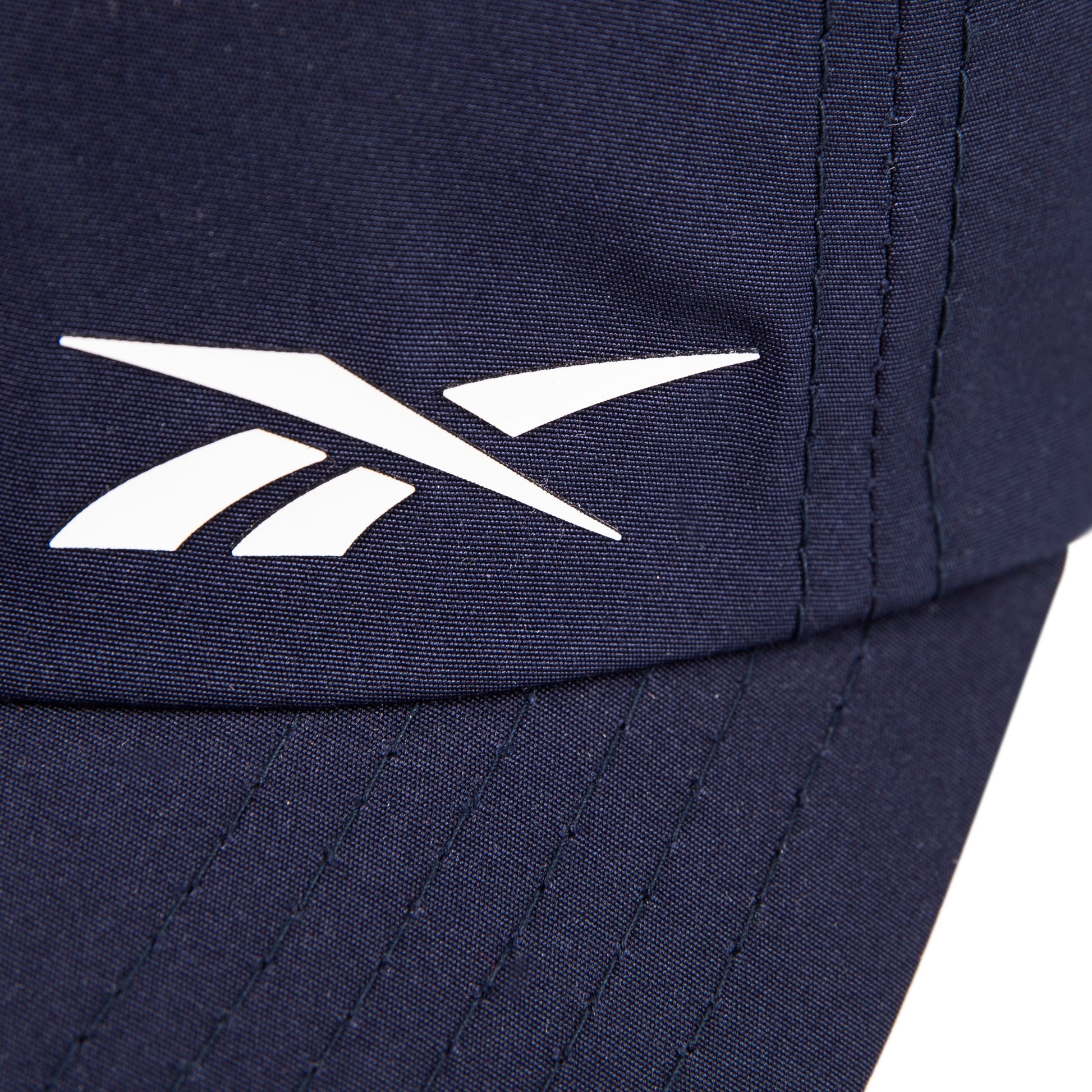 Close-up of the Reebok Flow Cap in navy blue, made from recycled polyester. Features a white Reebok logo near the stitched seam and a moisture-wicking sweatband for comfort.