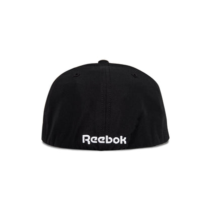The image shows the back view of the Reebok Range Cap, a black cap featuring the white embroidered Reebok logo near the bottom edge.