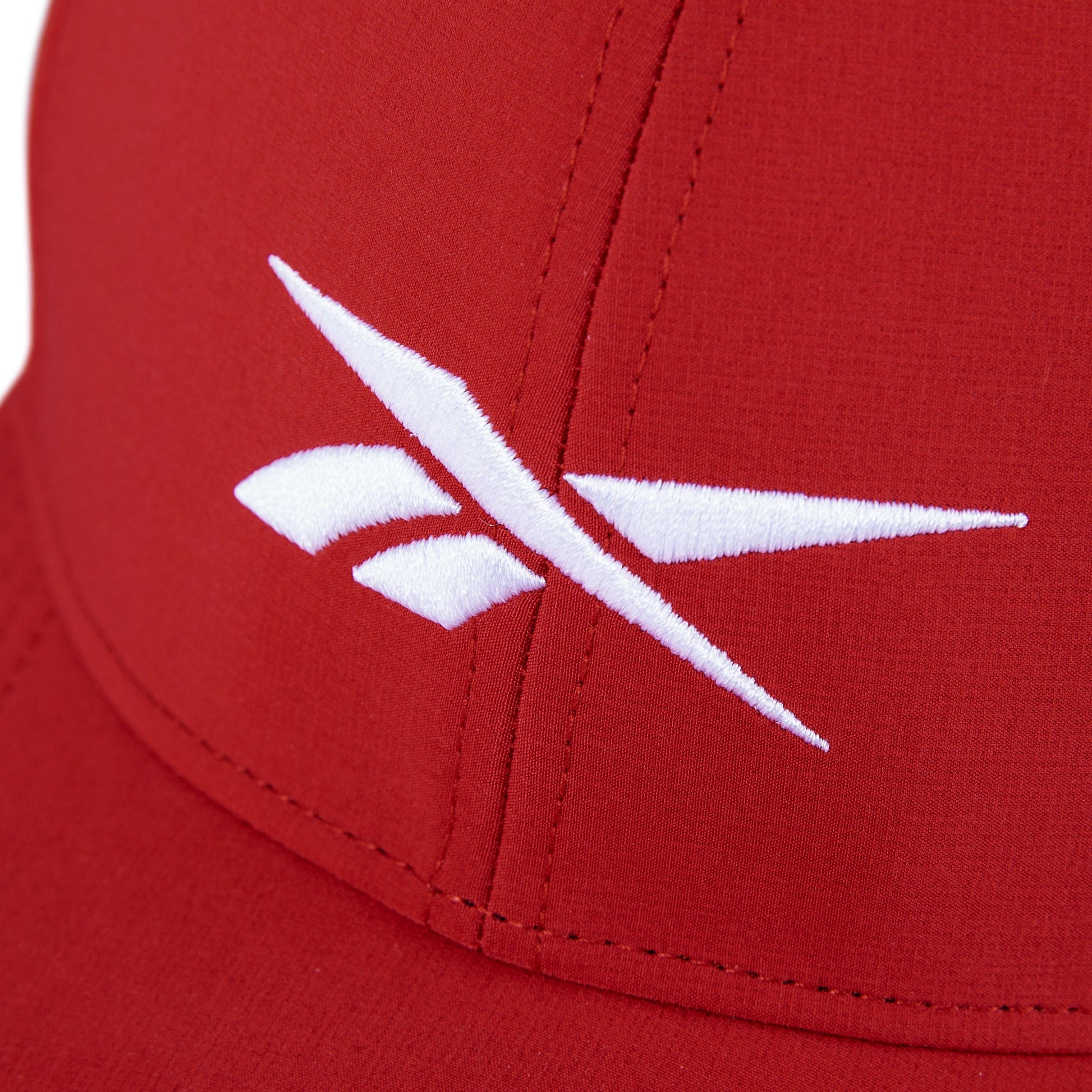 Close-up of the Reebok Range Cap, a red golf hat with a white embroidered logo of angled lines and shapes on the front panel, offering sun protection and moisture-wicking comfort.