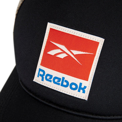 Close-up of the Reebok Vintage Trucker Cap with a stitched rectangular logo patch featuring blue lettering on a red background. The cap has a classic snapback closure for adjustable fit, reflecting Reebok’s athletic heritage.