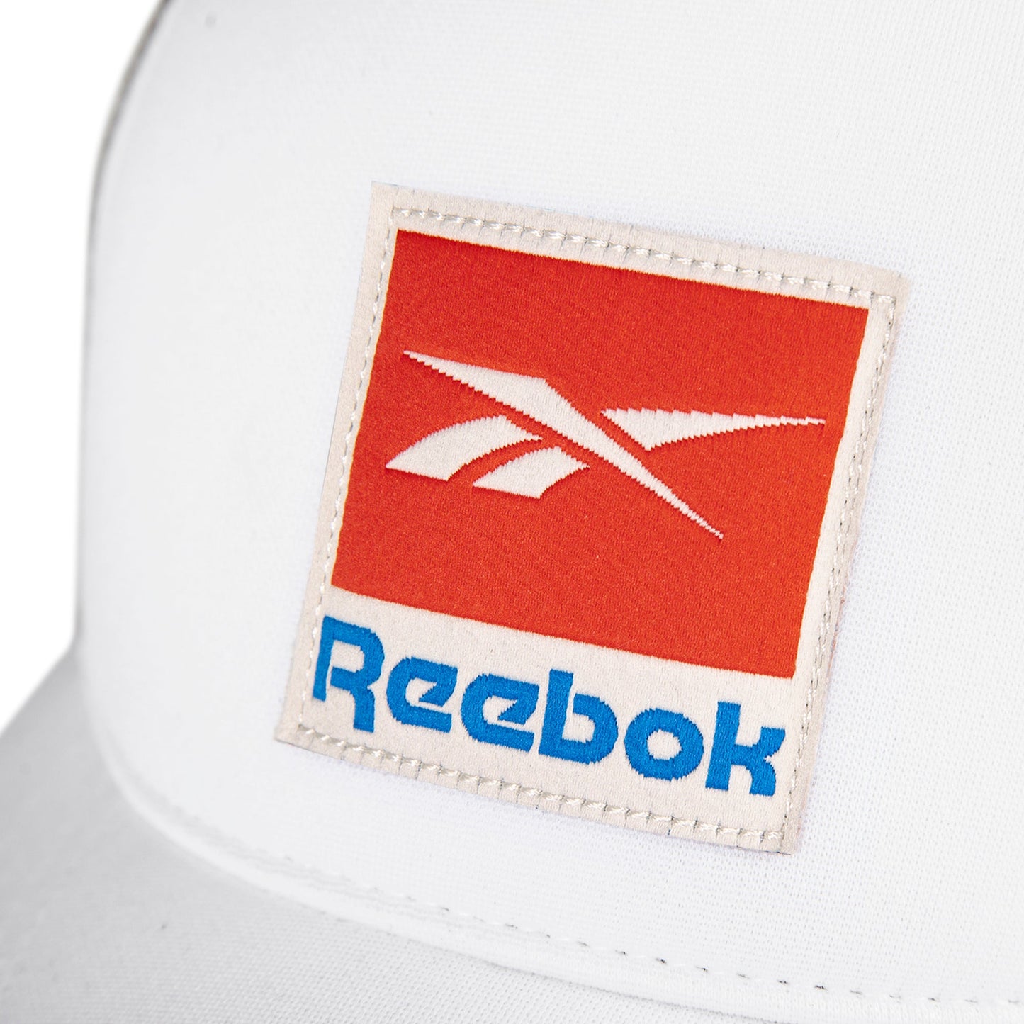 Close-up of the Reebok Vintage Trucker Cap in white, featuring a red and white Reebok logo patch, blue lettering, and a classic snapback closure for adjustable comfort.