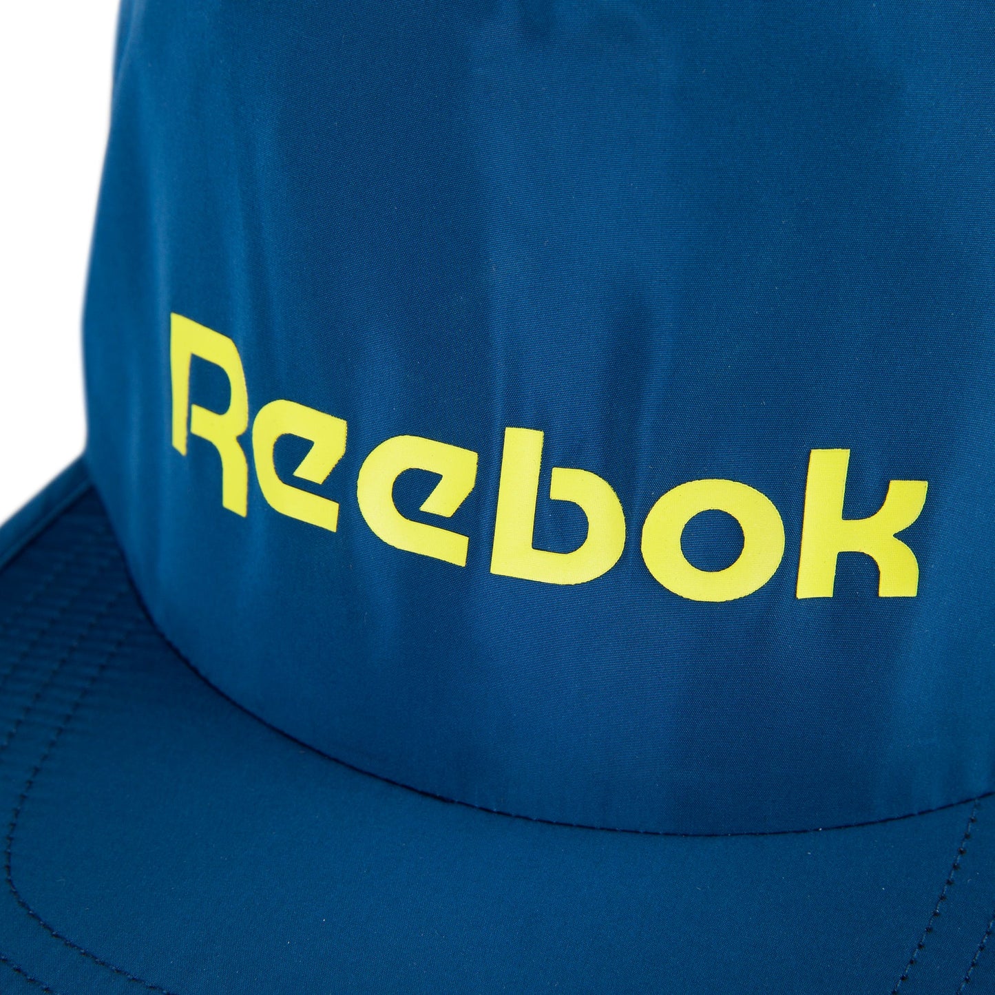 A close-up of the Reebok Flat Brim Running Cap in blue, featuring a yellow logo on the front. This lightweight cap uses moisture-wicking fabric to keep you cool and comfortable during workouts.