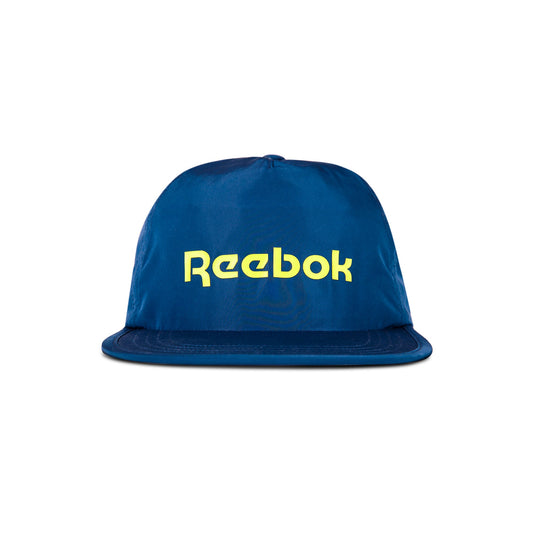 The Reebok Flat Brim Running Cap is a blue, lightweight hat with moisture-wicking fabric, featuring a flat brim and bold yellow Reebok logo on the front, shown against a white background.