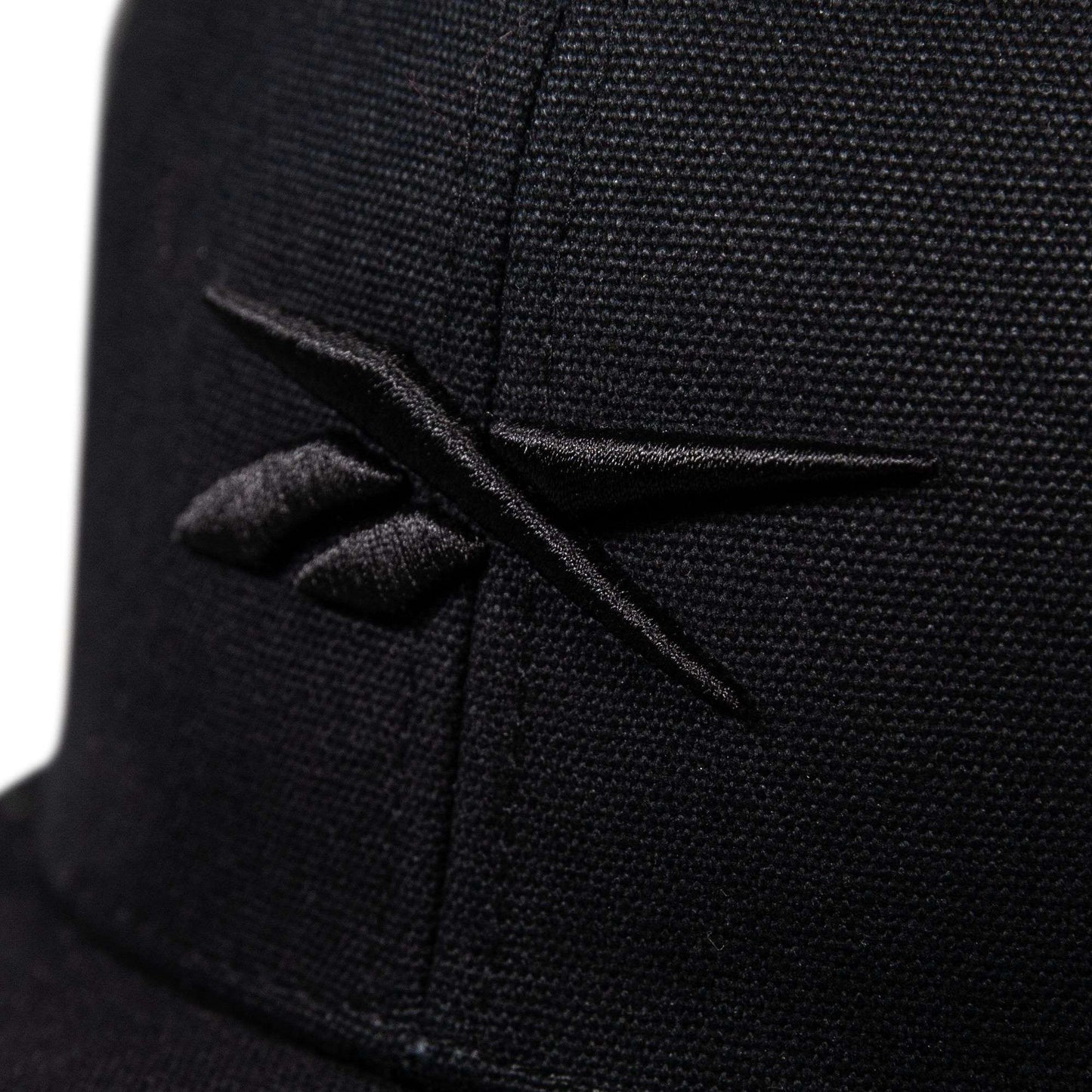 Close-up of the Reebok Embroidered Vector Trucker Cap in black, showcasing the embroidered black Reebok logo on the front with visible stitching and fabric texture.