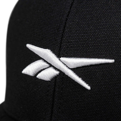 Close-up of the Reebok Embroidered Vector Trucker Cap, a black fabric hat with a white embroidered Reebok logo on the front.