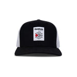 The Reebok Woven Patch Vector Trucker Cap features a black and white design, curved brim, mesh back, adjustable snapback, and a front woven patch with the Reebok logo plus a bold red accent.