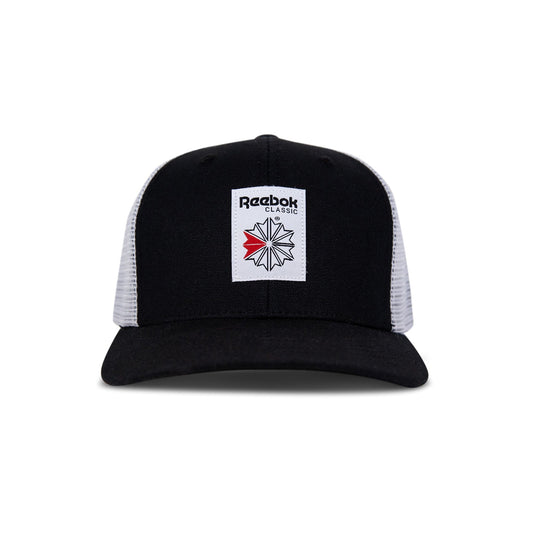 The Reebok Woven Patch Vector Trucker Cap features a black and white design, curved brim, mesh back, adjustable snapback, and a front woven patch with the Reebok logo plus a bold red accent.