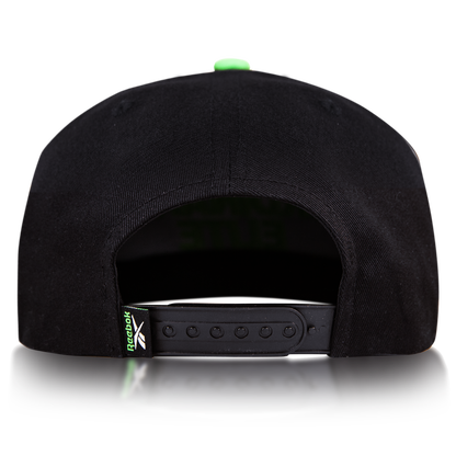Rear view of the Reebok Ordinary Elite Cap, featuring a cotton crown, adjustable snapback plastic strap, and a small green Reebok logo tag on the left side. Shown against a plain white background.