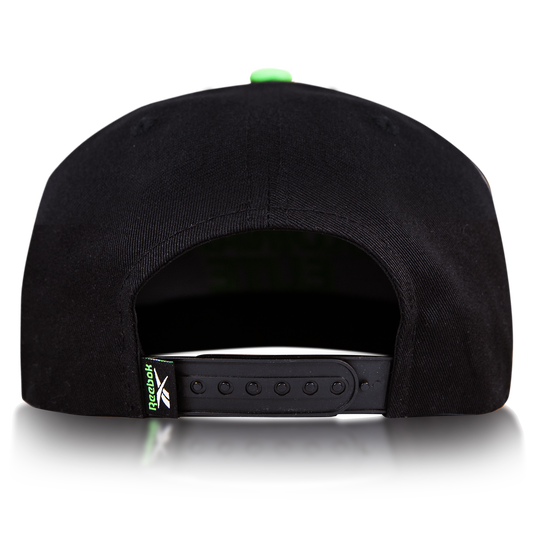Rear view of the Reebok Ordinary Elite Cap, featuring a cotton crown, adjustable snapback plastic strap, and a small green Reebok logo tag on the left side. Shown against a plain white background.