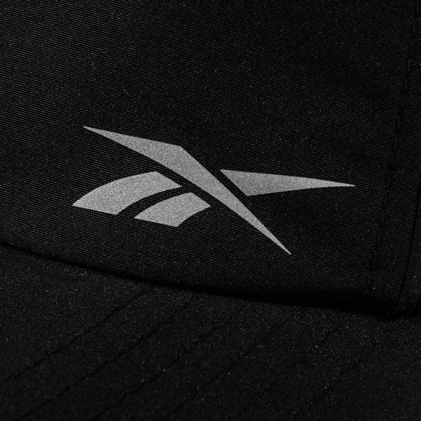 Close-up of a black Reebok Flow Piped Cap with a silver logo on the front and a moisture-wicking sweatband for all-day comfort.