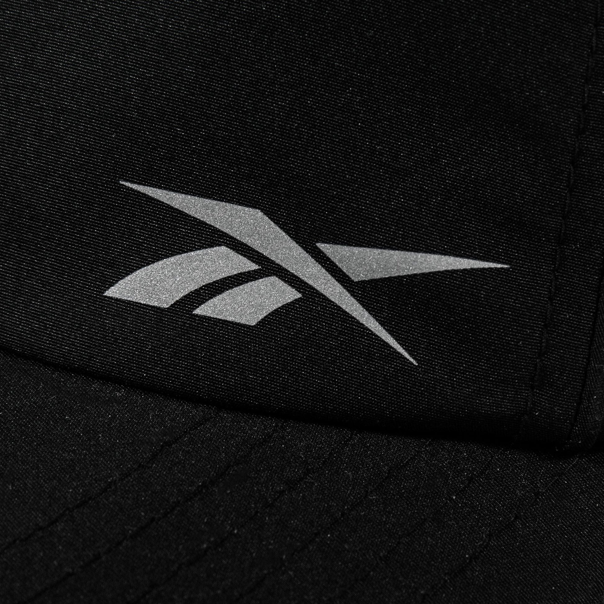 Close-up of a black Reebok Flow Piped Cap with a silver logo on the front and a moisture-wicking sweatband for all-day comfort.