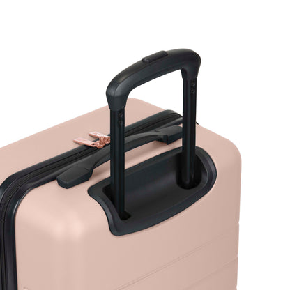 A close-up of a light pink hard-shell suitcase with a black telescopic handle extended and rose-gold zipper pulls.