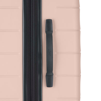 Close-up of a light pink hard-shell suitcase showing a vertical black zipper and a black handle on the right side. The suitcase surface has horizontal indented lines for texture.