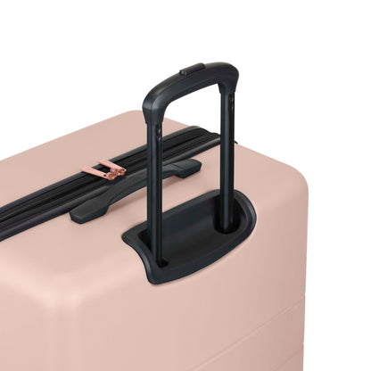 A close-up of a light pink hard-shell suitcase with a black telescopic handle extended and a zipper with rose gold accents.