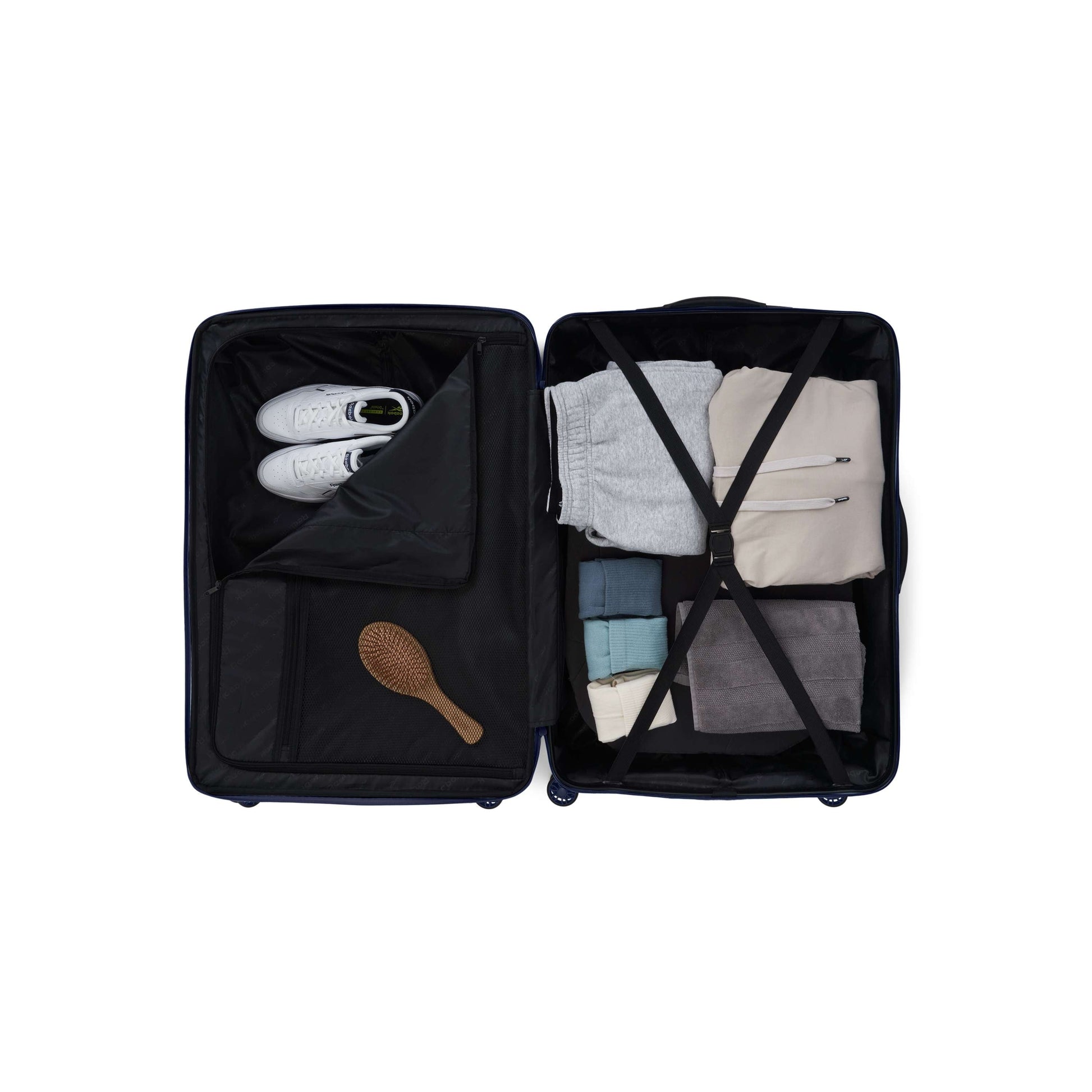 The Reebok Action Duo 2 Piece Luggage Set, featuring spinner wheels, opens to reveal neatly packed clothes, white sneakers, a wooden hairbrush, and folded garments secured with elastic cross-straps—organized and ready for travel.