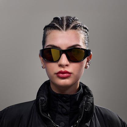A person with braided hair wears Reebok Nitrous Smart Audio Sunglasses with polarized lenses, a black high-collar jacket, earrings, and a chain necklace while posing against a plain gray background.