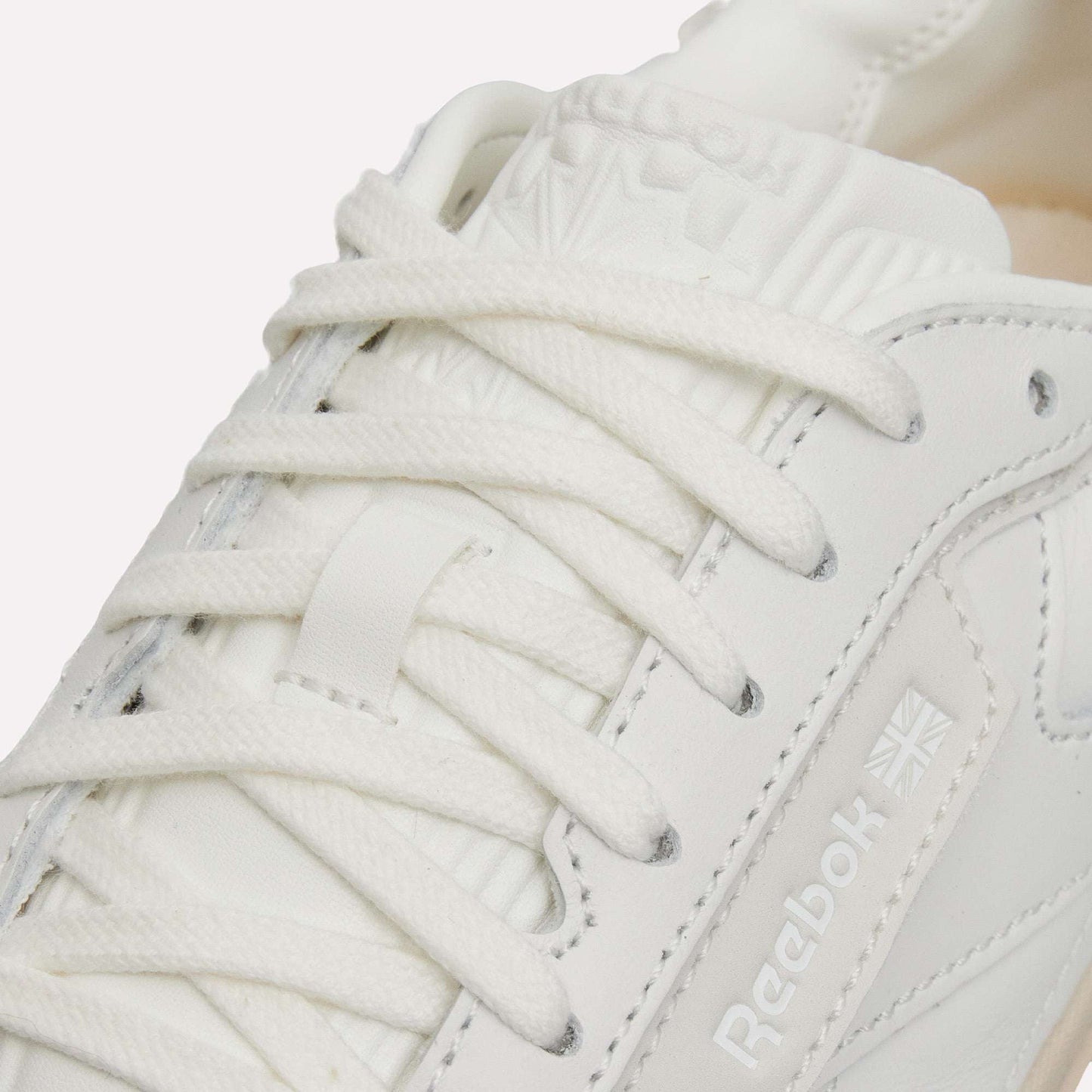 Close-up of the Reebok Club C LTD Shoes in white, highlighting laces, stitching, and the Reebok logo with a Union Jack. This classic lifestyle sneaker features smooth leather and a padded tongue, capturing timeless tennis-inspired style.