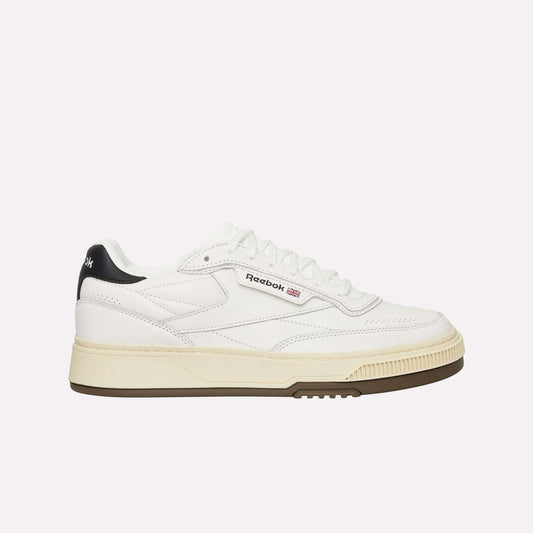 A white Reebok sneaker with a beige sole, black heel detail, and Reebok logo on the side, shown in a side profile on a plain white background.
