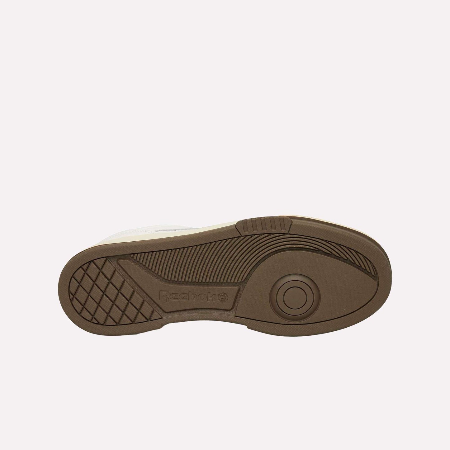 The image shows the brown rubber sole of a Reebok sneaker, viewed from the bottom, featuring textured grip patterns and the Reebok logo embossed near the heel. The sole is set against a plain white background.