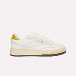 The Reebok Club C LTD Shoes feature a white upper, gold heel and logo accents, a beige midsole, and a brown outsole. Shown on a light blue background, these classic tennis sneakers offer timeless style.