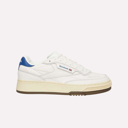 The Reebok Club C LTD Shoes are classic white tennis shoes with a blue heel detail, beige midsole, brown outsole, and feature the Reebok logo plus a small Union Jack flag on the side.