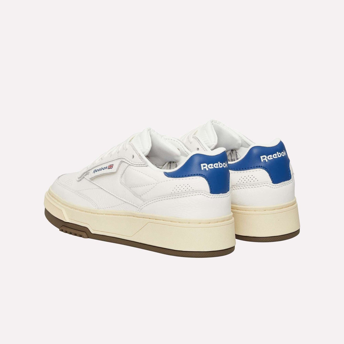 A pair of Reebok Club C LTD Shoes in white with beige soles and blue heel tabs, displayed from back and side angles on a plain white background.