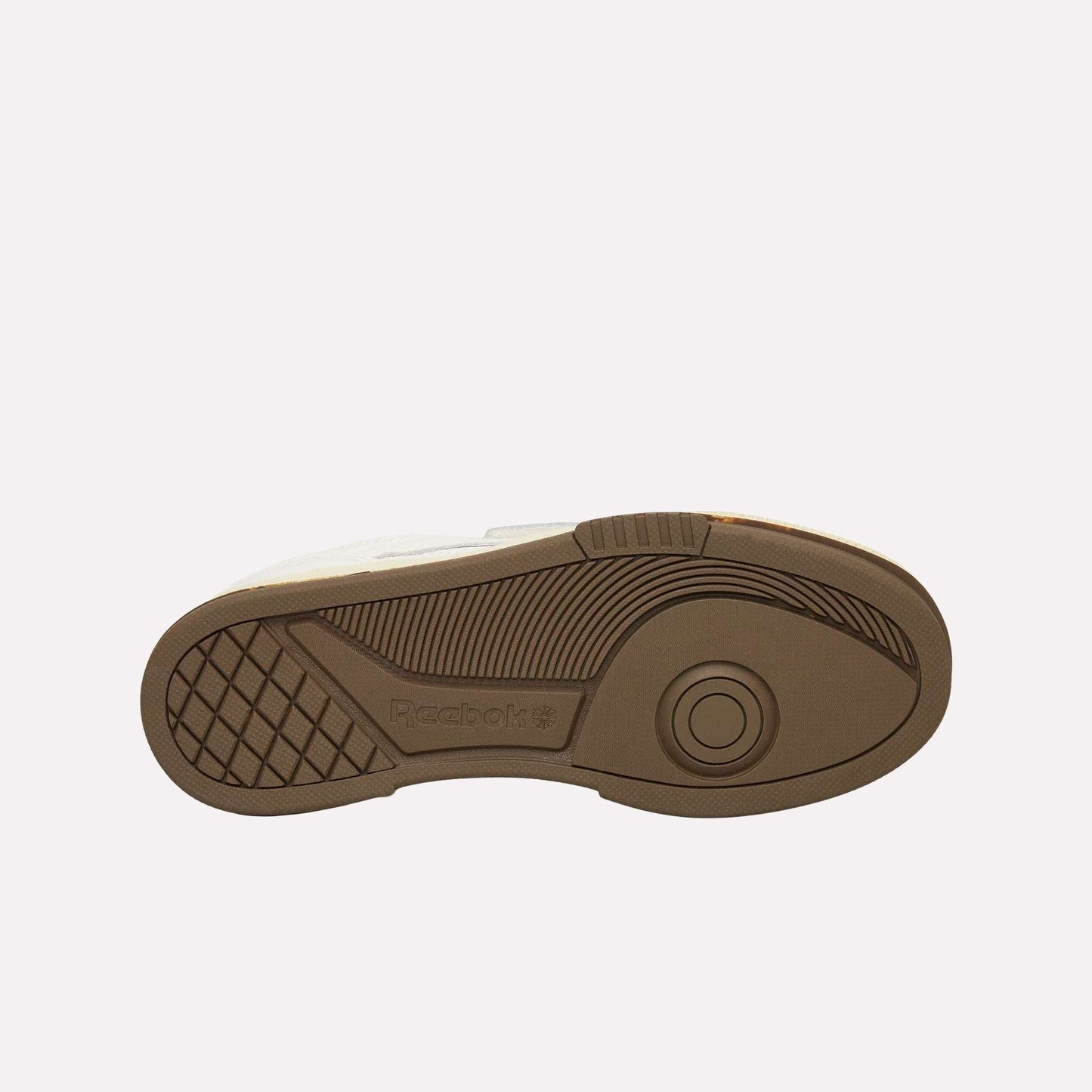 The image displays the brown rubber outsole of the Reebok Club C LTD Shoes with textured tread patterns, including circular and linear designs for traction, plus an embossed Reebok logo near the heel.