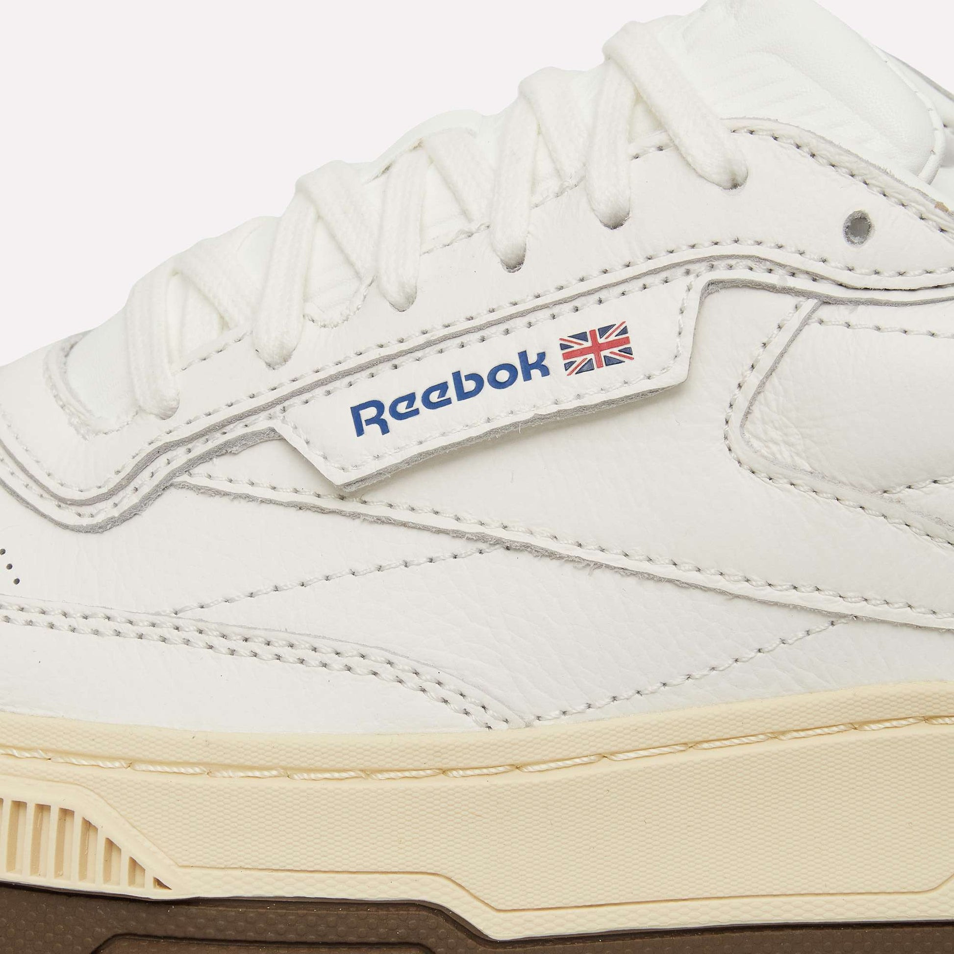 Close-up of a white Reebok Club C LTD shoe with textured leather, white laces, beige midsole, brown outsole, and the iconic Reebok logo—an updated take on this classic lifestyle sneaker.