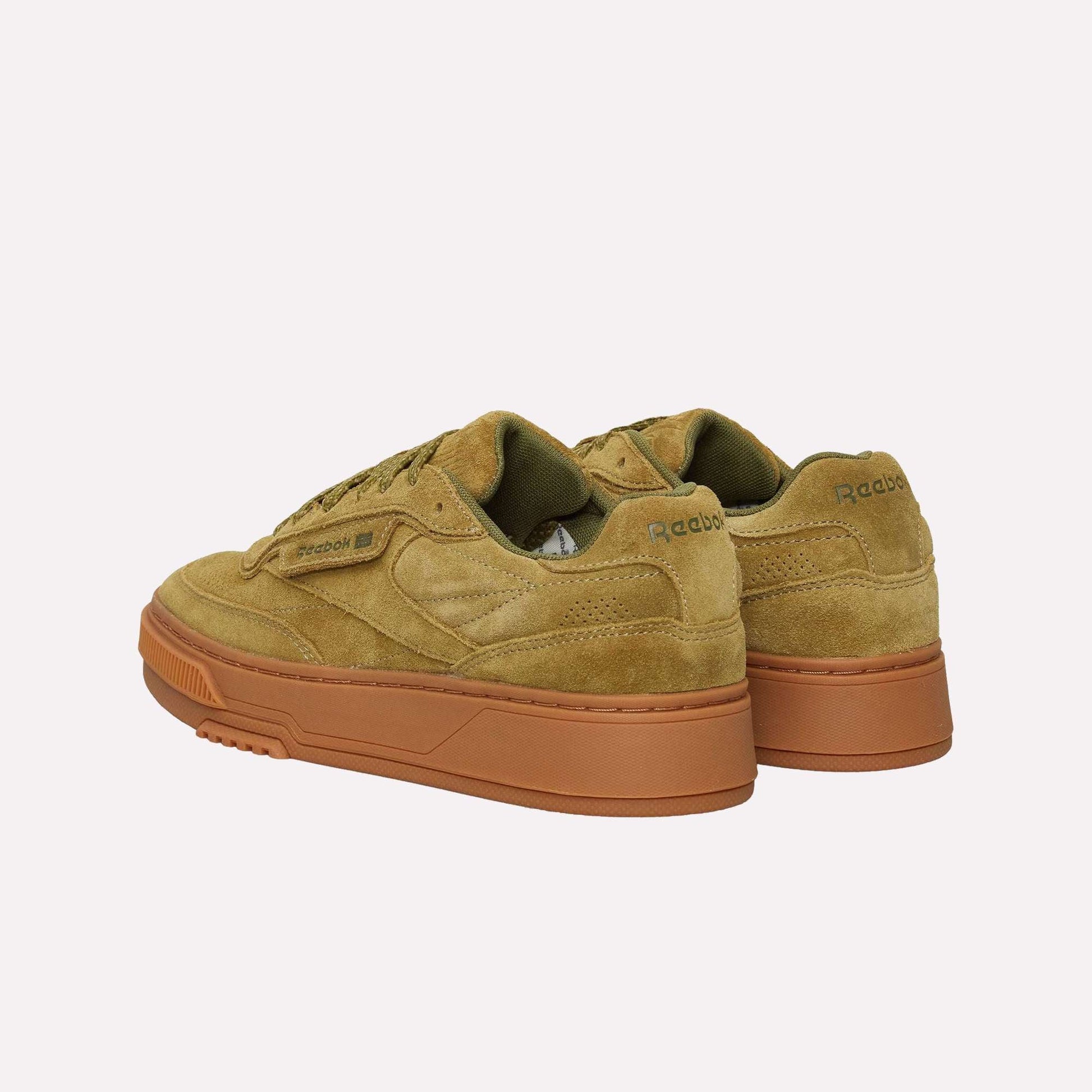 The Reebok Club C LTD Shoes in olive green suede feature dark green accents and chunky gum rubber soles, blending classic style with modern tennis-inspired details—shown from an angled rear view.