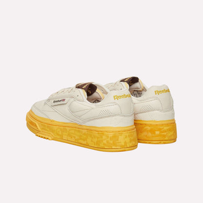 The Reebok Club C LTD Shoes feature a cream upper, yellow patterned soles, brown tongue labels, a yellow Reebok logo on the back, and black and red details on the side for a classic lifestyle look.