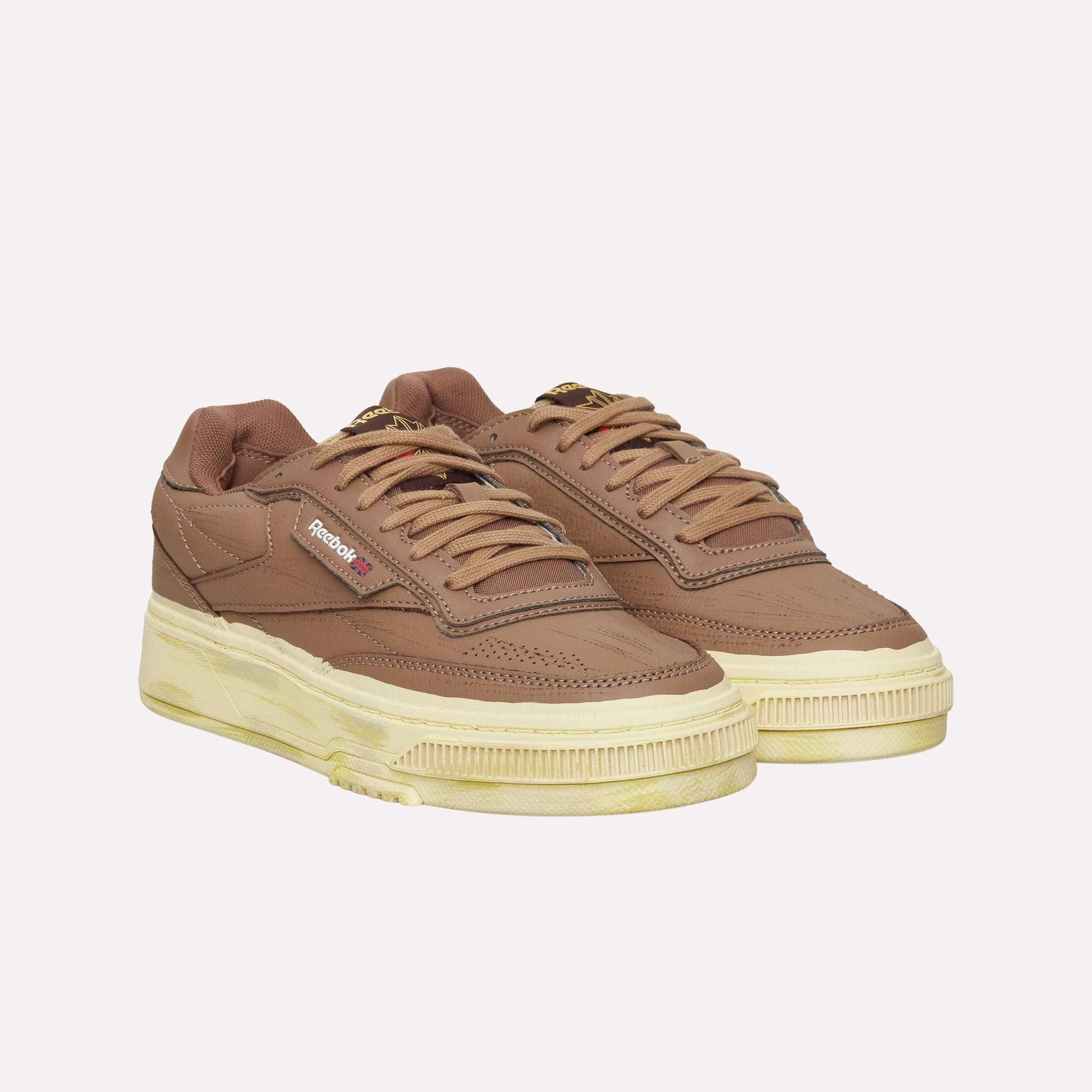 The Reebok Club C LTD Shoes, in brown with beige, vintage-look soles, feature laces and the signature logo on the side. Displayed against a white background, these sneakers offer a classic blend of comfort and timeless style.