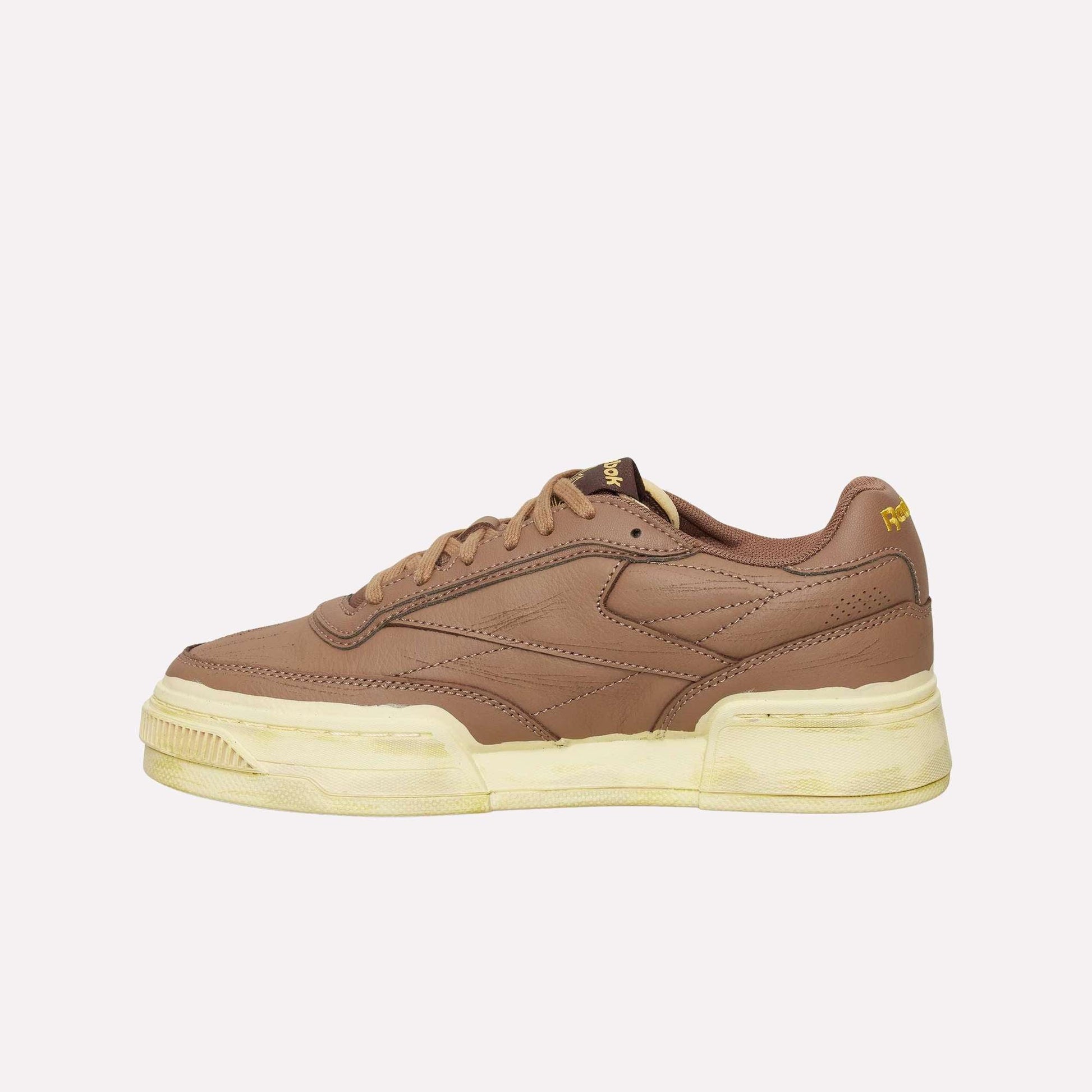 The Reebok Club C LTD Shoes feature brown leather, a thick off-white sole, subtle stitching, a low-top design, and yellow Reebok branding near the heel and tongue—perfect for a classic lifestyle look.