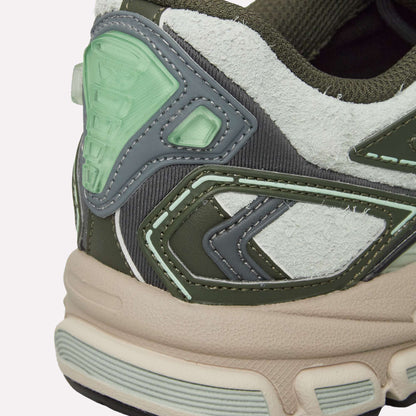 Close-up of the heel of Reebok Premier Road Ultra Shoes, featuring textured white, green, and gray panels with pale green accents and a beige dual-density midsole, set against a light blue background.
