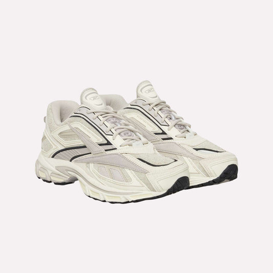 A pair of Reebok Premier Road Ultra Shoes in off-white with black accents and thick dual-density midsoles, displayed side by side on a light blue background.