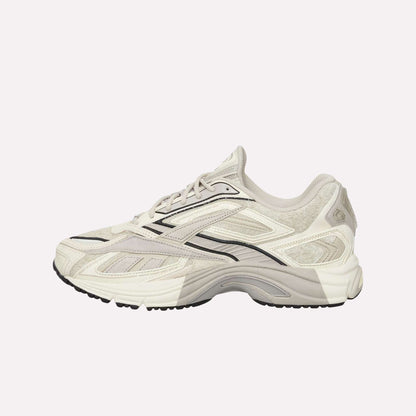 The Reebok Premier Road Ultra Shoes feature a beige and white upper with black accents, lace-up closure, textured details, patterned sole, and a dual-density midsole for comfort. Shown in side profile on a light blue background.