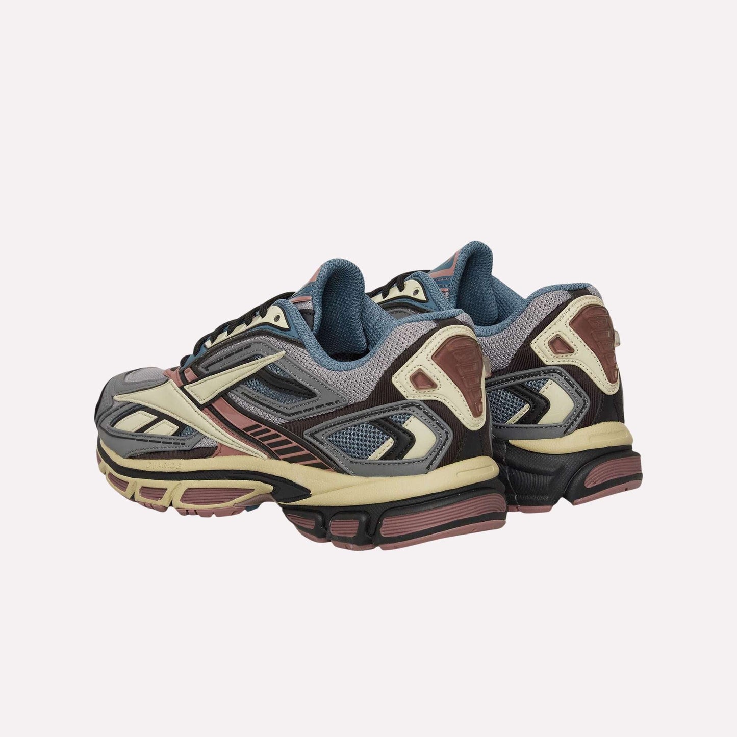 The Reebok Premier Road Ultra Shoes feature a blend of gray, cream, pink, and black with mesh panels and chunky dual-density midsoles, displayed against a light blue background.