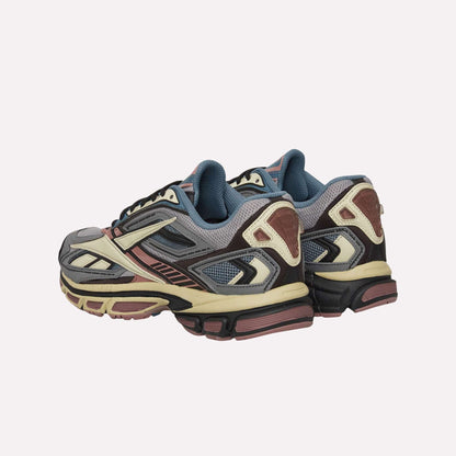 The Reebok Premier Road Ultra Shoes feature a blend of gray, cream, pink, and black with mesh panels and chunky dual-density midsoles, displayed against a light blue background.