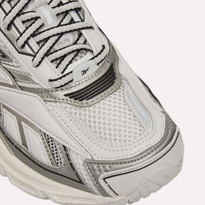 Close-up of white and silver Reebok Premier Road Ultra Shoes, featuring mesh and leather details, dual-density midsole, black and white laces, stitched patterns, and a small Reebok logo on the tongue.