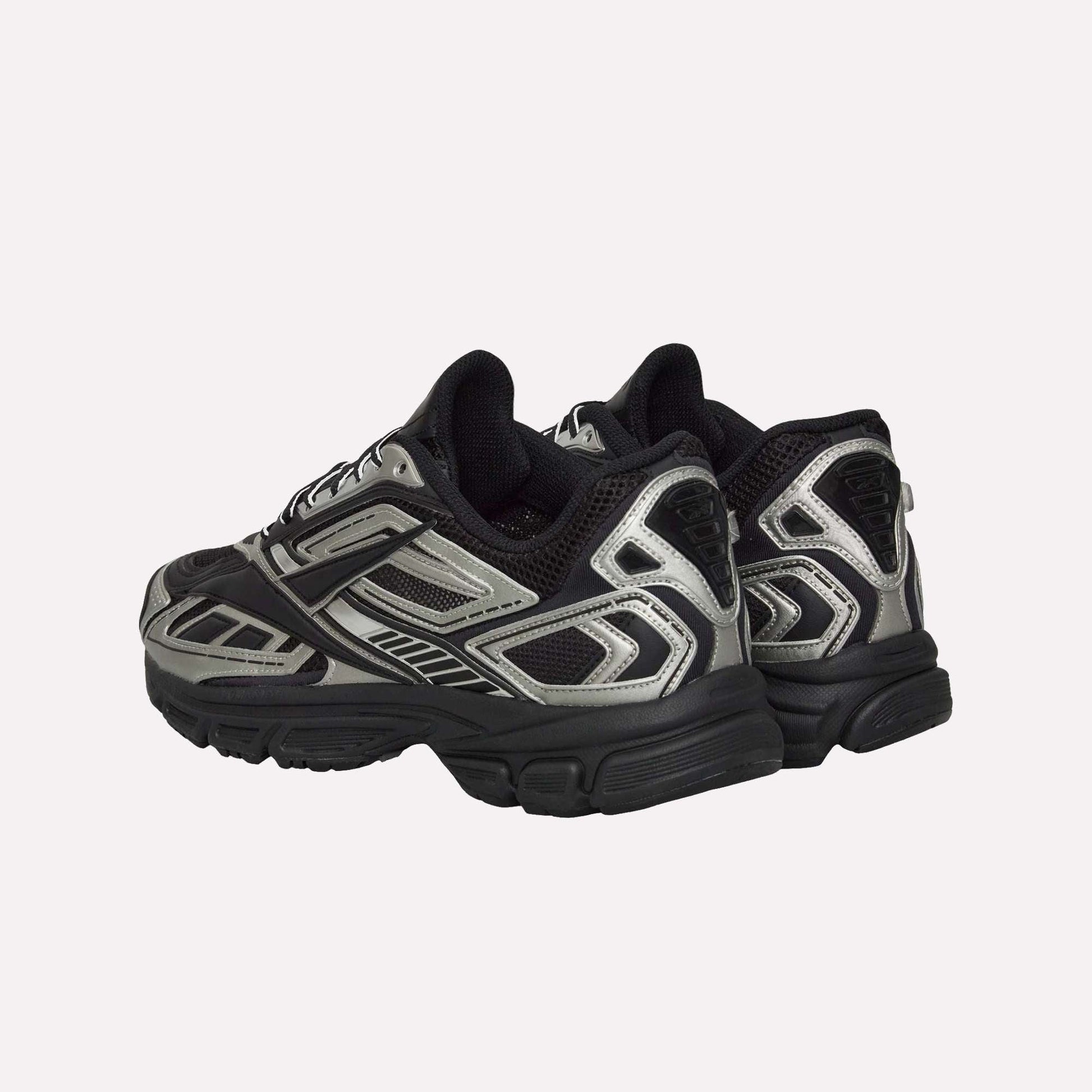 The Reebok Premier Road Ultra Shoes are chunky athletic running sneakers with silver, black, and grey panels, seen from back and side angles, featuring a dual-density midsole, thick soles, and mesh detailing.