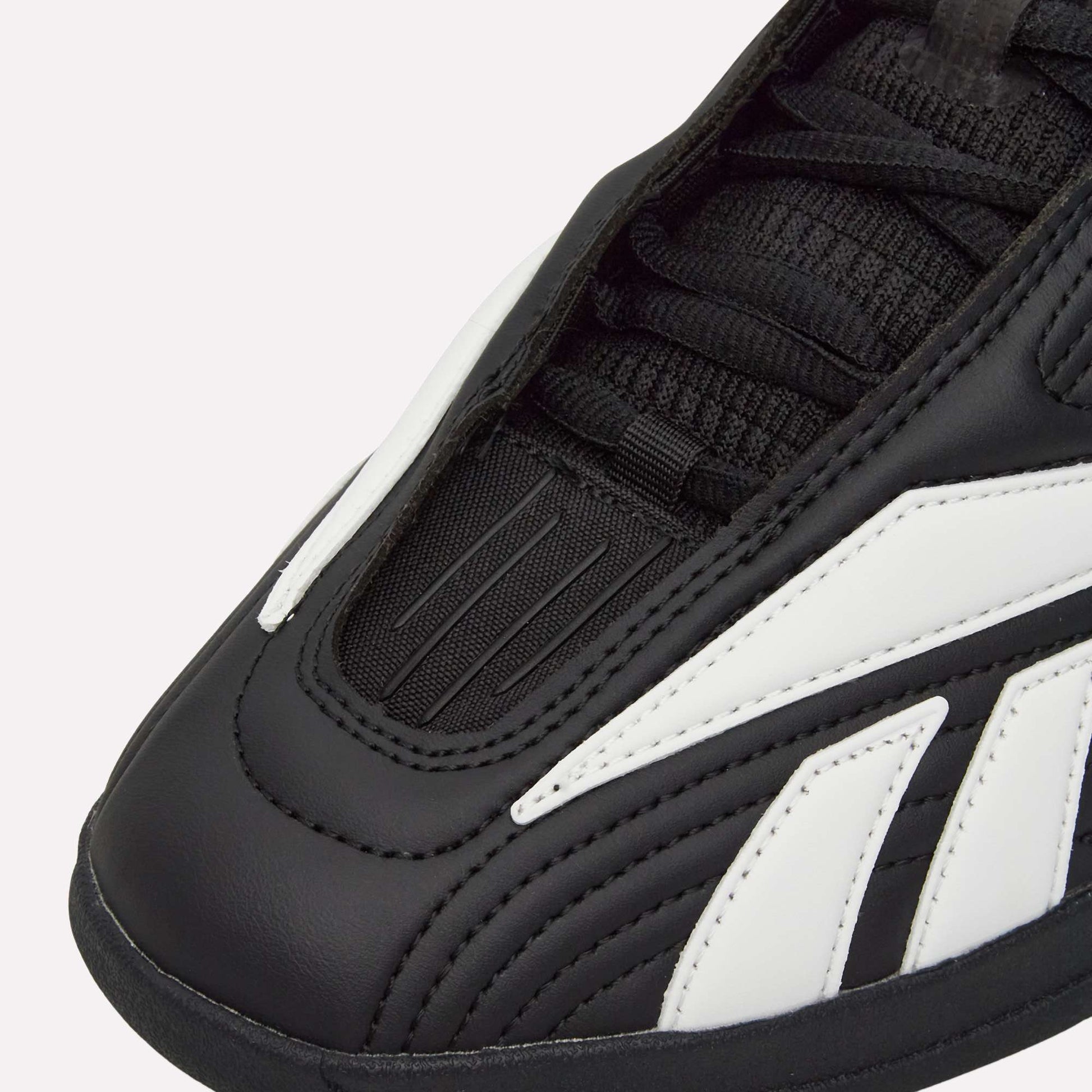 Close-up of Reebok Hammer Pro LTD Shoes in black with white accents, highlighting detailed stitching, laces, textured faux leather upper, and a durable rubber sole.