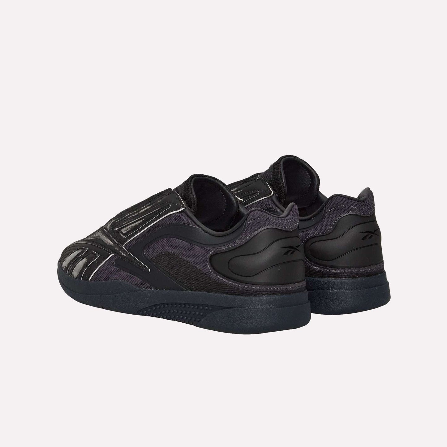 A pair of Reebok Hammer Pro LTD Shoes in black, featuring a faux leather upper, textured rubber sole, and reflective silver accents, shown from back and side angles on a white background.