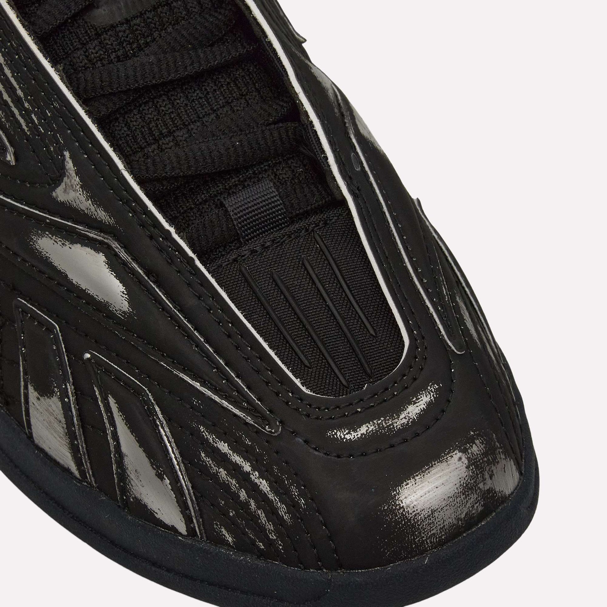 Close-up of the front and side of Reebok Hammer Pro LTD Shoes in black, featuring a shiny, textured faux leather upper with black laces and detailed stitched and grooved designs on the material.
