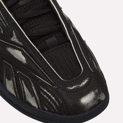 Close-up of the front and side of Reebok Hammer Pro LTD Shoes in black, featuring a shiny, textured faux leather upper with black laces and detailed stitched and grooved designs on the material.