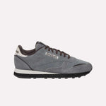 The Reebok Classic Leather Premium LTD Shoes feature a gray upper, black laces, a white and black sole, and a white heel accent—showcasing their retro-inspired silhouette against a light blue backdrop.