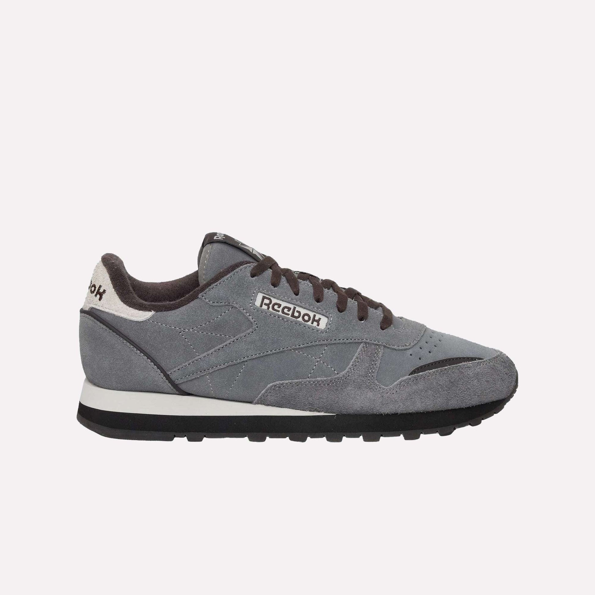 The Reebok Classic Leather Premium LTD Shoes feature a gray upper, black laces, a white and black sole, and a white heel accent—showcasing their retro-inspired silhouette against a light blue backdrop.