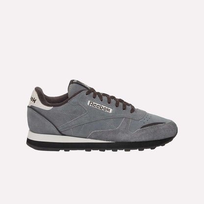 The Reebok Classic Leather Premium LTD Shoes feature a gray upper, black laces, a white and black sole, and a white heel accent—showcasing their retro-inspired silhouette against a light blue backdrop.