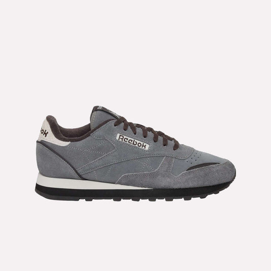 The Reebok Classic Leather Premium LTD Shoes feature a gray upper, black laces, a white and black sole, and a white heel accent—showcasing their retro-inspired silhouette against a light blue backdrop.