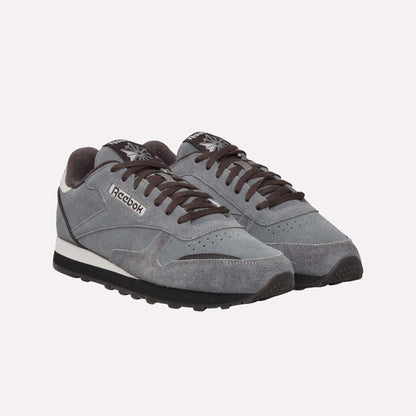 A pair of gray Reebok Classic Leather Premium LTD Shoes with black laces and soles, white midsoles, and suede uppers, featuring a classic silhouette on a light blue background.